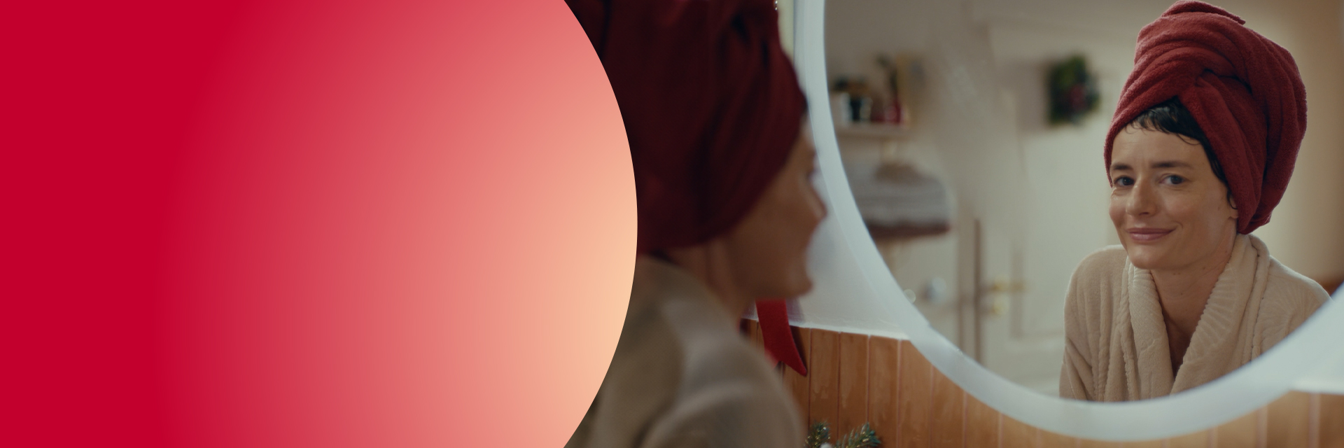 Uśmiechnięta kobieta znajdująca się w łazience, patrząca w lustro, z turbanem z ręcznika na głowie - znajdź chwilę dla siebie.