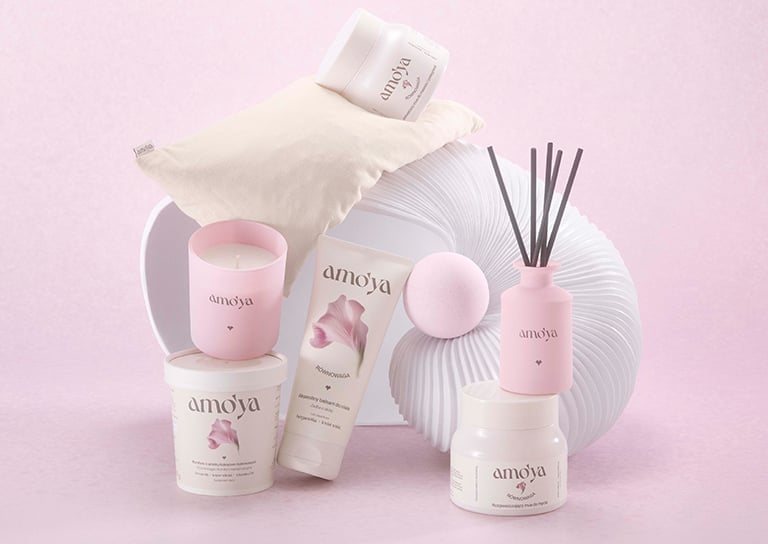 Produkty AmoYa Równowaga na różowym tle: kremy, balsam do ciała, świeca zapachowa i dyfuzor – banner drogerii Rossmann.