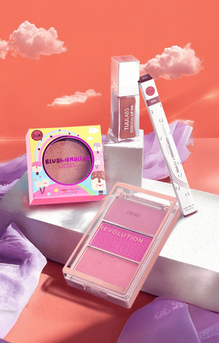 Paleta różów Revolution, olejek do ust Tulilabs, róż Blush Mallow i pisak do stylizacji brwi J. Cat na artystycznym tle z chmurami.